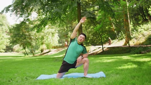 Adult Asian Sportsman Guy Does Gymnastics Practices Yoga Performs Exercises on Mat in City Park