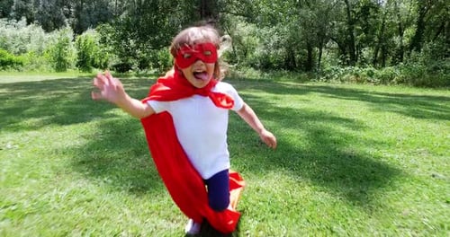 lovely free little girl play dressed as a comic book hero, runs happily in a beautiful garden . fr
