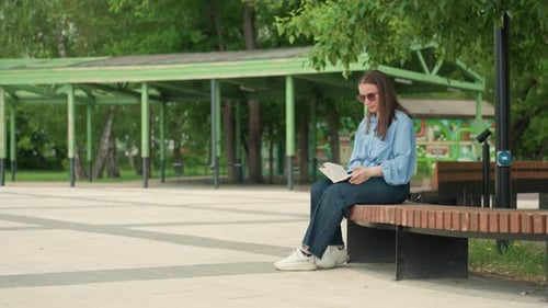 Woman Reading Book on Bench in Urban Park