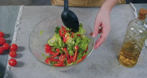 Top view of woman hands which mixing fresh vegetable salad applying spoon in transparent bowl