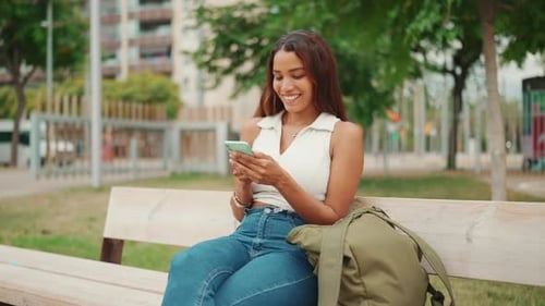 Woman Using Phone on Park Bench in City