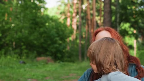 Madre lleva a una niña con expresión triste en un bosque verde