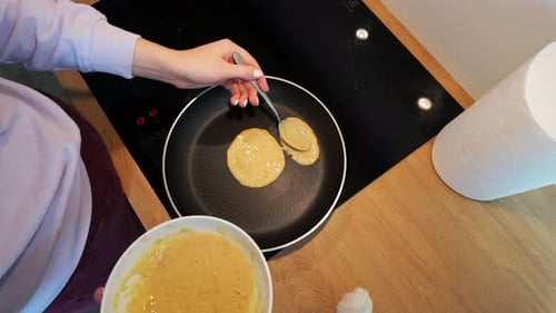 Aufnahme von oben nach unten einer Frau, die morgens in der Küche zu Hause Pfannkuchen zum Frühstück zubereitet