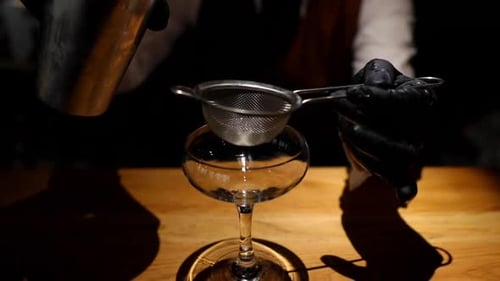 Bartender pouring drink from shaker into glass over deep ready to serve final drink closeup view of