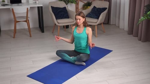 Young Woman Practicing Yoga at Home on Blue Yoga Mat