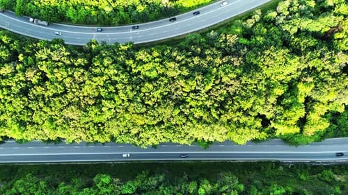 Two roads with cars moving by. Wooded countryside crossed by the highways. Top view.