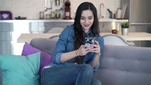 Woman uses smartphone sitting on sofa at home