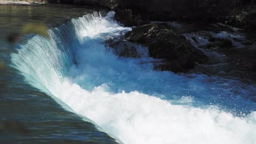 Close-up of a cascading waterfall, with water flowing smoothly over rocky ledges into a pool below.