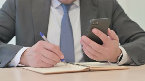 Close Up of Businessman Writing Information from Smartphone