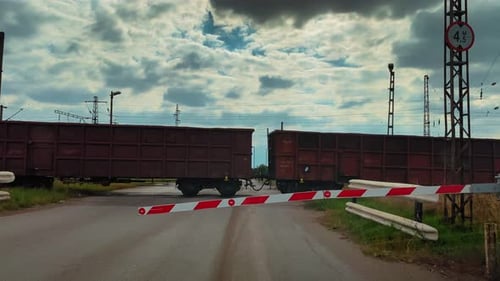 un train traverse un passage à niveau aux barrières abaissées (ciel théâtral)