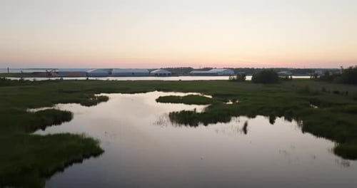 Aerial view over marchlands with buildings in the background, summer sunset