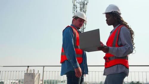 Team young engineer walking inspection construction site and talking while looking laptop.