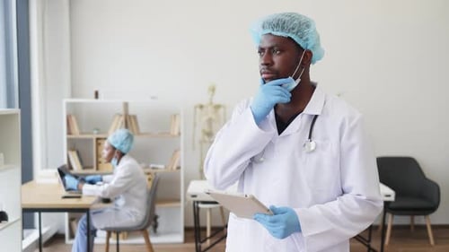 Doctor Reviewing Patient Data on Tablet While Colleague Works in Medical Office