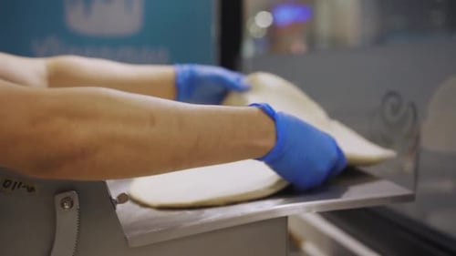 Baker Flattening Dough On Machine Inside The Bakery. - close up