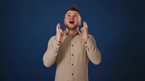 Hopeful Wish Man Crossing Fingers for Luck on Blue Background