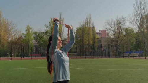 Young Woman Uses Resistance Band For Her Exercise At the Stadium