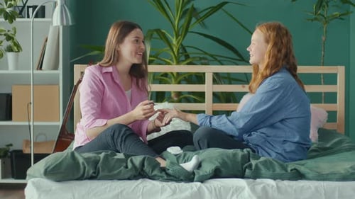 Girlfriends Students Sit at Home on Bed and Paint Nails