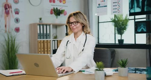 Portrait of woman doctor in glasses and hospital uniform which typing on computer in medical workr