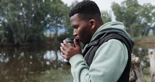 Young Adult Drinks from Mug Near Lake