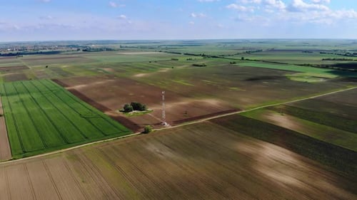 Flying over a cellphone tower on the field on a sunny day