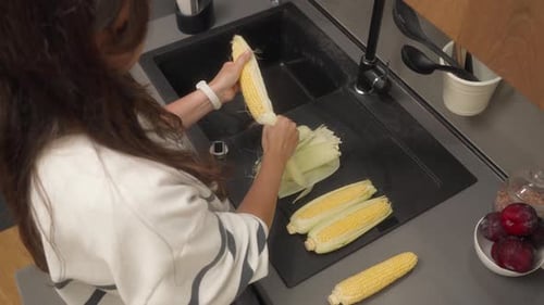 Young Adult Peels Corn in Kitchen