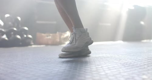 Jumping in white sneakers, man exercising in gym with sunlight streaming in