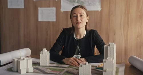 Woman Works on Designs and Sketches at Her Desk in an Office Surrounded By Small Building Models