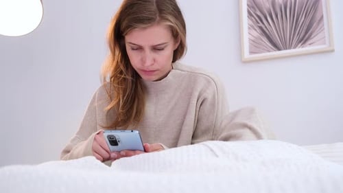 Young Woman Using Smartphone While Relaxing on Bed