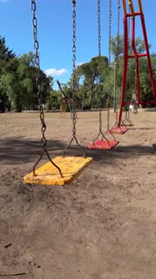 Old empty swings in a children's park with a dirt floor. Vertical shot.