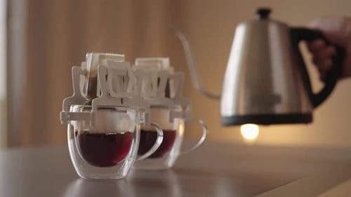 Closeup Side View of Male Hand Pouring Hot Water From Gooseneck Kettle Into Disposable Drip Coffee