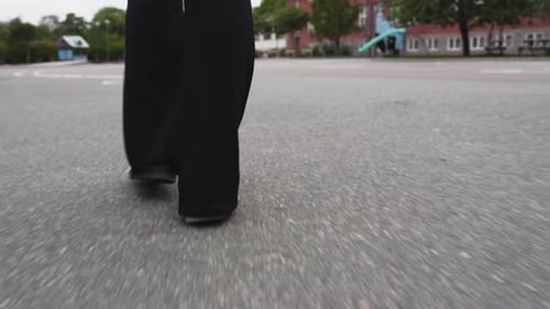 Closeup moving footage following the feet of a female walking on a school yard on asphalt.