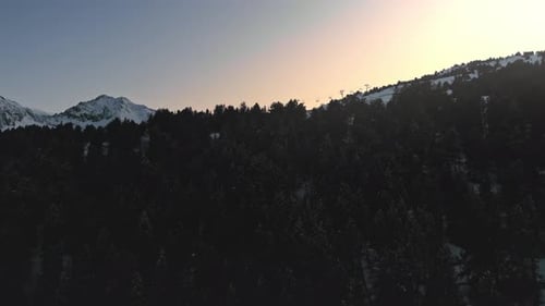 Aerial pullback, ski lift at a ski resort on alpine snowy mountain during golden hour