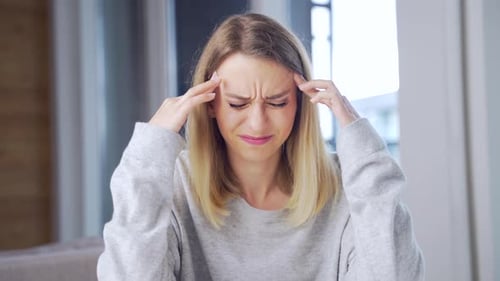 Portrait of a young blonde woman sitting at a table in the office or at home and holding his head