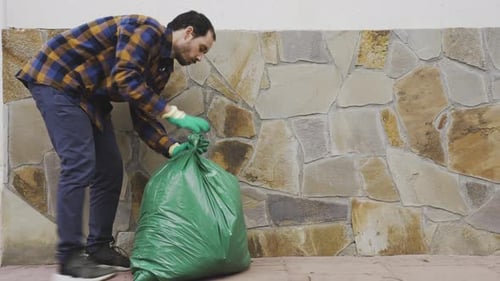 hombre caucásico recogiendo basura pesada bolsa de basura llena de residuos biológicos de alimentos, botella reciclable