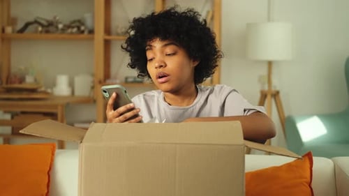 Woman With Phone Unpacks Box at Home