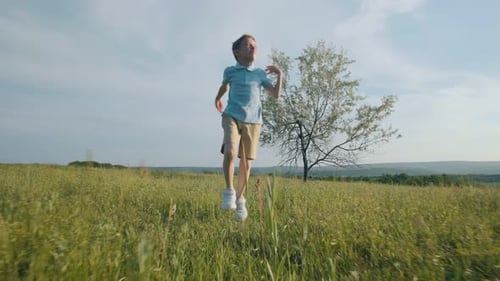 Front View of Boy Running and Jumping Freely Through Grassy Field