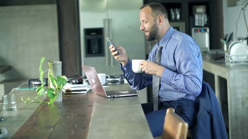 Man Works from Home Drinking Coffee with Phone