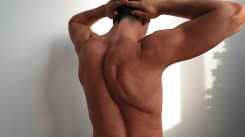 Man Flexing Back Muscles Against White Wall