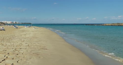 Low altitude drone forward flight over sandy beach with gentle waves in Protaras Cyprus