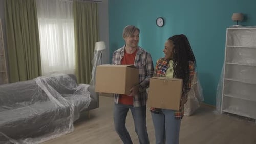 Young Couple with Cardboard Boxes in Their Hands in a New Apartment A Man and an African American