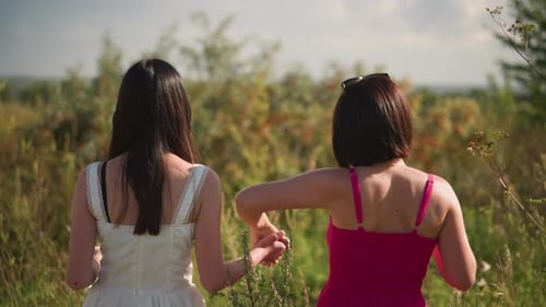 Two Women Walk Holding Hands Through a Field