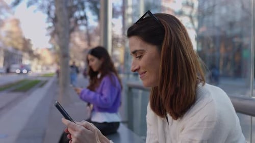 Two Young Women Using Smart Phone Waiting at Tram Station Platform