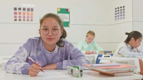 Teen Student Writing at Desk in Classroom