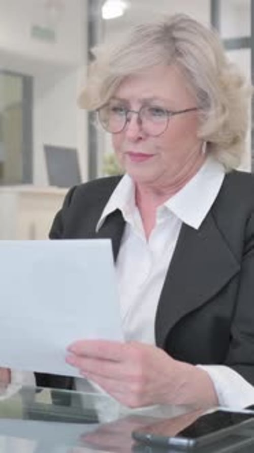 Thoughtful Woman Reads Documents at Desk in Office