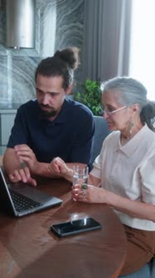 Un tuteur technique expliquant les bases d'un ordinateur portable à une femme âgée à la maison