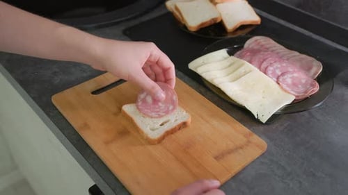 Hand Selecting Slice of Salami From Black Plate with Deli Meats and Cheese Beside Bread on Wooden