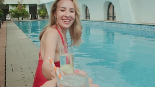 Femme tintant des lunettes avec une amie au bord de la piscine en vacances
