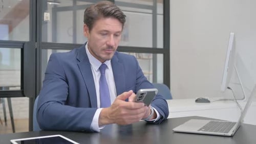 Businessman Using Smartphone at Desk in Office
