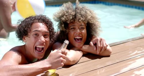 Smiling Diverse friends enjoying pool party, holding drinks and relaxing by water
