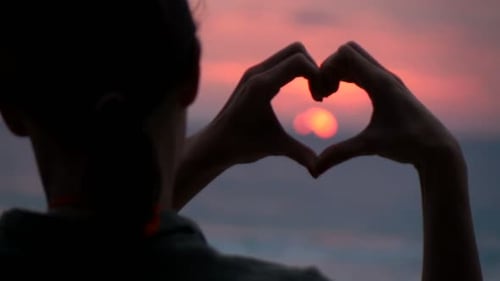 Woman Making Heart Symbol With Her Hands During Sunset On Beach